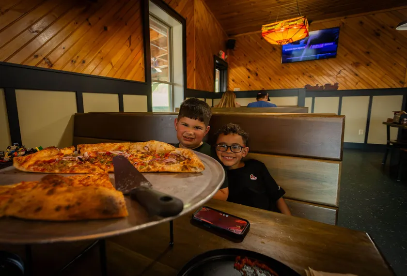 Two young guests grinning over a fresh pie in a booth