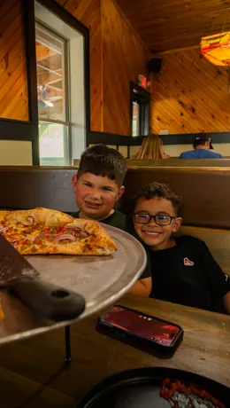 Two young guests grinning over a fresh pie in a booth