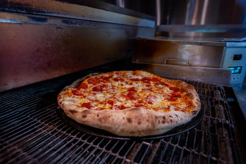 A pepperoni pie coming off the oven deck